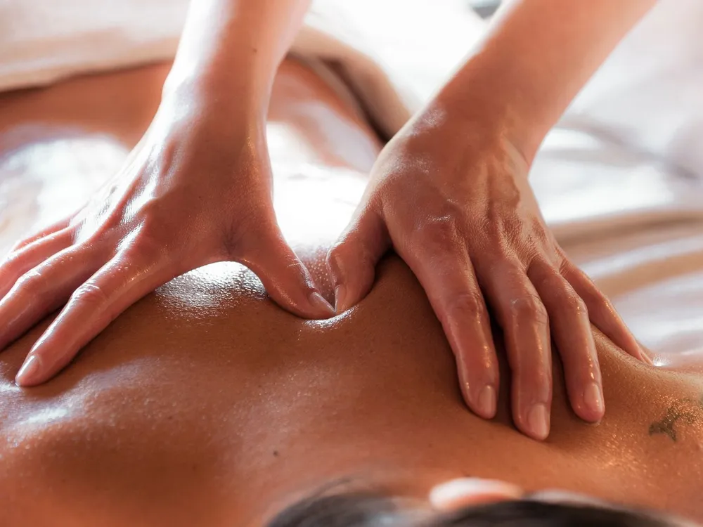 Two hands applying firm pressure with oil on the upper back during massage