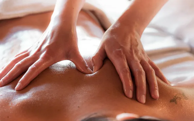 Two hands applying firm pressure with oil on the upper back during massage