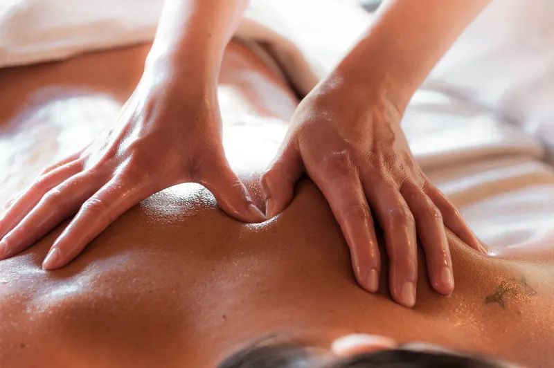 Two hands applying firm pressure with oil on the upper back during massage