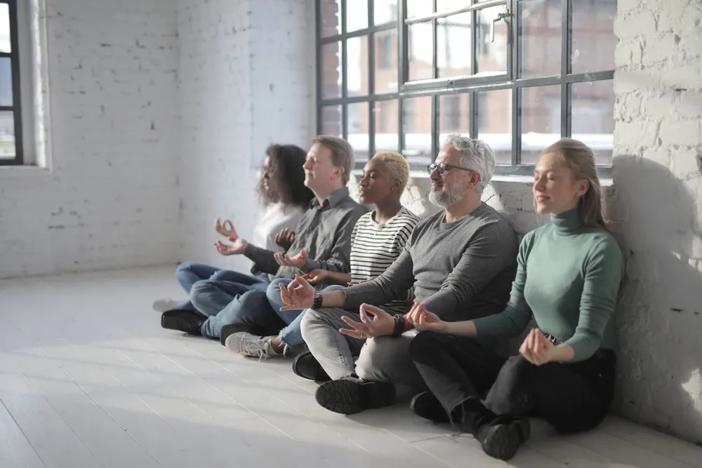 Five colleagues sitting cross-legged in a meditation session in a bright office