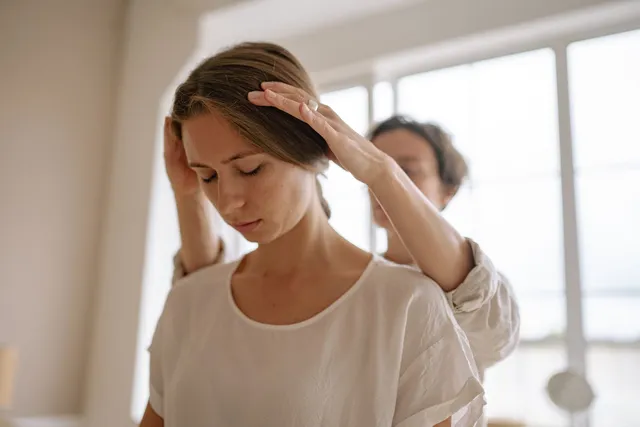 Woman with eyes closed receiving a gentle scalp massage from a therapist standing behind her